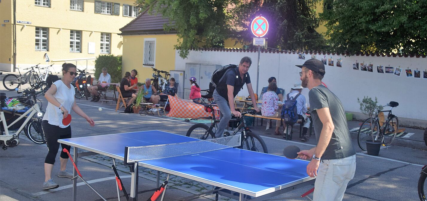 Tischtennispartie und Menschen im Hintergrund, die am Straßenrand sitzen.