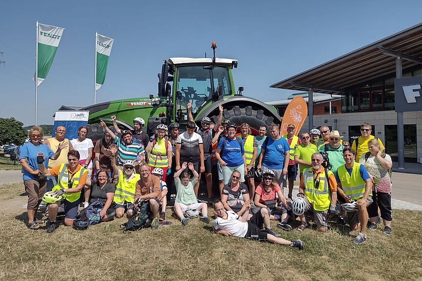 Mittagspause am Fendt-Forum Menschen winken auf einer Wiese vor einem großen grünen Traktor
